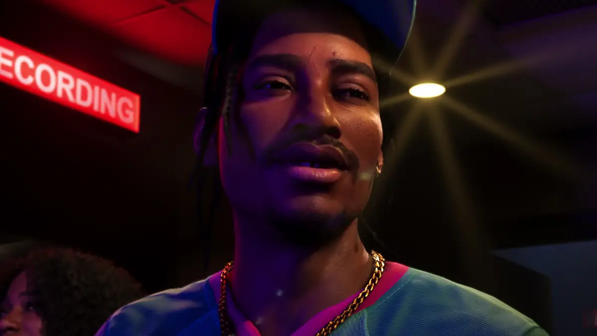 a man in a cap and gold chain under a red recording sign in a dim studio in an official GTA 6 screenshot
